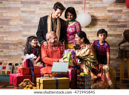 Indian family celebrating diwali festival or birthday by exchanging gifts, 3 generations of indian family and gifts and sweets, happiness concept
