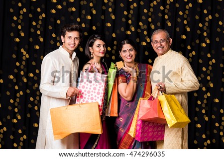 portrait of cheerful indian family with shopping bags in traditional wear in diwali isolated over black background