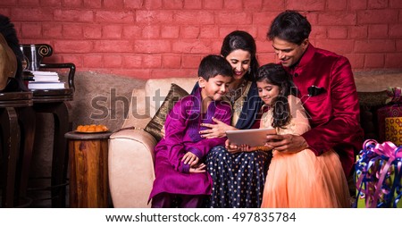 Smiling Indian family on the sofa using technology or tablet or tab or mobile, Indian family shopping online on diwali / taking selfie using tablet or mobile, people celebrating diwali with technology