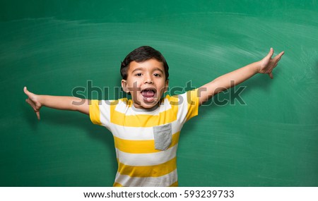 Indian school kid in hand stretched pose over green chalkboard or chalk board background, indian boy standing over green background in school