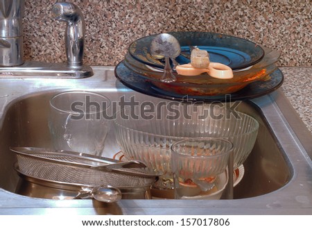 Close up of the kitchen sink with very messy piles of dirty dishes. The sink is stainless steel. The dishes are bowls, plates, pans and flatwear. Concept of disorganization and clutter and filth