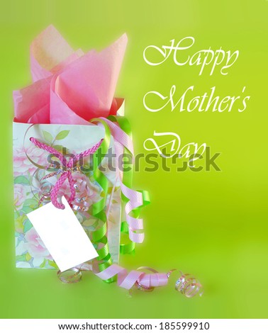 A cheerful gift bag and ribbons with a blank card for mother\'\'s day. The floral bag is pink and green. There is pink tissue paper and ribbons, all on an apple green background. Vertical composition