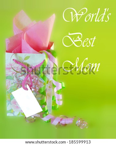 A cheerful gift bag and ribbons with a blank card for mother''s day. The floral bag is pink and green. There is pink tissue paper and ribbons, all on an apple green background. Vertical composition