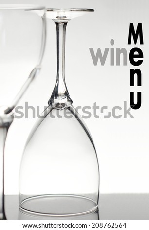 Two backlit empty wine glasses with text for wine menu. The glass closest to viewer is cropped and out of focus, the distant glass is focused and upside down. The text for wine menu is grey and black