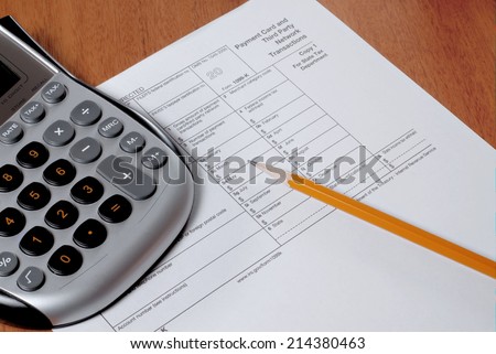 IRS form 1099, a calculator and a sharpened pencil on a wooden desk. The 1009 form is used to record and track the earnings of a freelancer or independent contractor, not a regular employee.