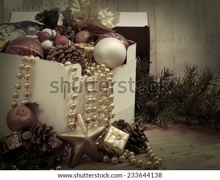 Opened box with a variety of Christmas decorations spilling out with vintage, instagram style filter applied.  Decorations include Christmas balls, beads, pine-cones, silk décor and a gold star