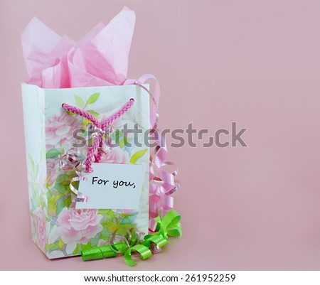 Pink and green are the main colors in this gift bag decorated with spring flowers. There is pink tissue paper showing from inside the bag. There are matching pink and green ribbons and a message