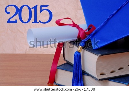 2015 message next to detail of blue cap and tassel and diploma tied with red ribbon, both resting on a stack of old books on a wooden desktop. Rough textured background that is neutral in color