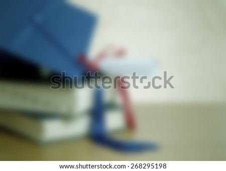 background blur graduation image includes stacked books, blue mortarboard cap with tassel and diploma tied with red ribbon. Not date or year specific, generic application. Horizontal composition
