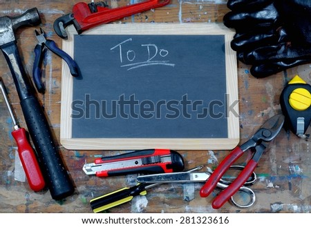 Dad\'s to do list is blank and nothing is written on a blackboard on paint stained table with various tools surrounding including a hammer, scissors, screwdriver, plum bob, box cutter and wrench.