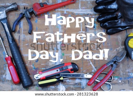 Happy Father\'s Day message on a paint stained work surface with tools scattered around. Tools include hammer, screwdrivers, wrench, snipper, plumb bob, gloves, box cutter and scissors.