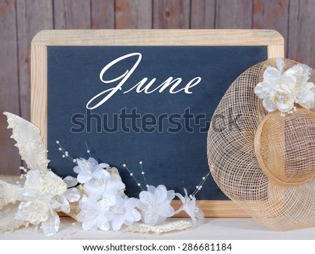 Month of the year image of blackboard in front of wood background with thematic decorations all in warm color tones. Month is June. Bridal and anniversary decorations added. Space for your date.