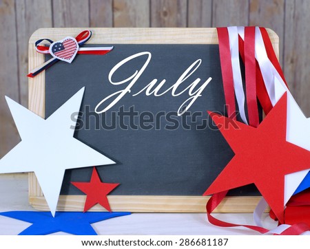 Month of the year image of blackboard in front of wood background with thematic decorations all in warm color tones. Month is July. Patriotic red white and blue decorations. Space for your date