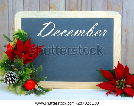 Month of the year for December with seasonally correct items placed around a blackboard with the month written across the top. There is a rustic wood background and copy space on the blackboard.