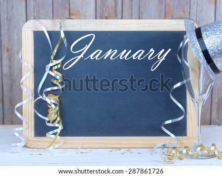 Month of the year for January with seasonally correct items placed around a blackboard with the month written across the top. There is a rustic wood background and copy space on the blackboard.