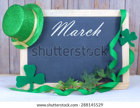Month of the year for March with seasonally correct items placed around a blackboard with the month written across the top. There is a rustic wood background and copy space on the blackboard.