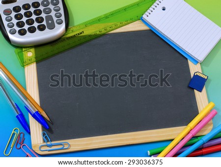 Back to school or office supplies surrounding a blank slate board on background that is green on top, fading to blue. Supplies include paper clips, pencil, pen, notepad, markers. Center copy space.