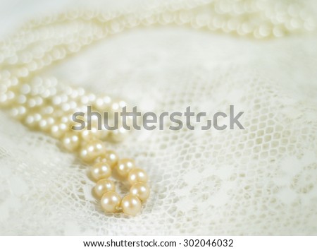 Two strands of pearls on lace with vintage filter applied.  One strand has a deeper ivory color, one strand is a brighter, lighter color. Good bokeh. Horizontal image with copy space
