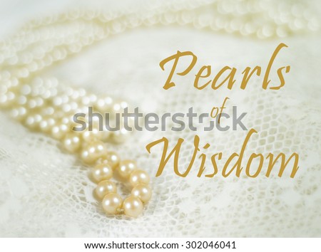 Two strands of pearls on lace with vintage filter applied.  One strand has a deeper ivory color, one strand is a brighter, lighter color. Good bokeh. Common phrase pearls of wisdom is added