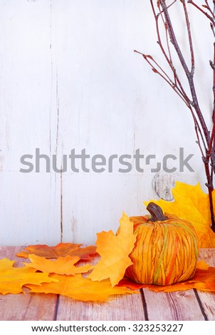 Decorative pumpkin, fall leaves and bare branches on wood table in front of whitewashed rustic wooden background. Gold, yellow and orange colors. Copy space on left. Good for fall or Halloween.