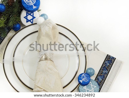 Place setting using white china dishes with black and gold trim topped with a sparkly napkin in a silver ring tied with a white bow. Evergreen and blue and white decorations for Hanukkah. Copyspace