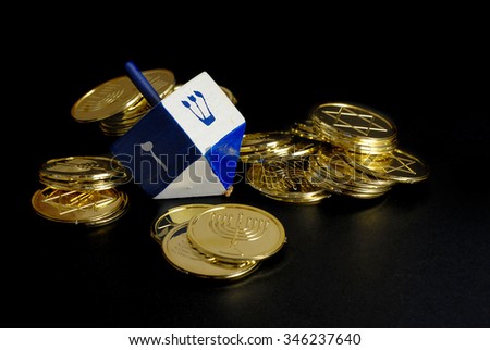 Low key image with dramatic side lighting of Hanukkah dreidel and gelt. Objects are on a rough, black background. Dreidel symbols are shin to put one in and gimmel to take all. Narrow depth of field.