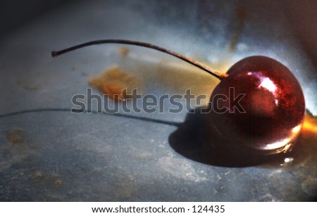 A single bing cherry in a pewter bowl laying in it\'s own juices.  There is strong side lighting that casts a shadow on the pewter surface.  Image was shot with a horizontal orientation