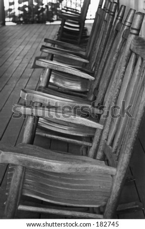 Several vintage wooden rocking chairs lined up on a wood porch. This monotone, black and white image is of a vintage front porch at a West Palm Beach, Florida museum called Yesteryear Village