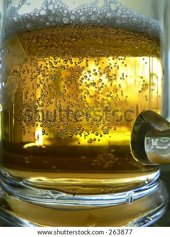 Close up of a schooner of beer that has just been drunk from. The bubbles from the carbonation are visible and the beer suds is not at the top of the mug. There is bright light shining through.