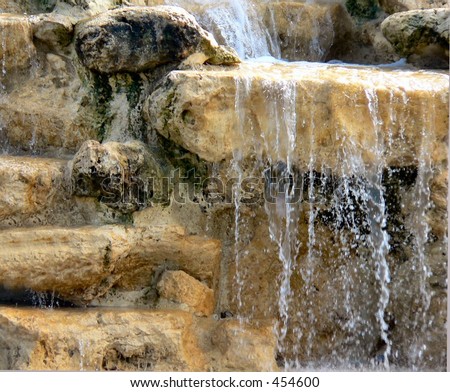 Close up detail of a sunshine splashed waterfall. The water mostly coming over the right side of the image, cascading over a boulder located in upper right corner.  Left side is more dry.
