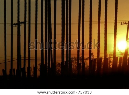 rebar at construction sight power lines crossing perpendicular silhouetted on orange sunset sky