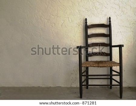 Vintage ladder back chair next to blank wall in late afternoon sun. The wall is stucco. The chair sits to the right of the image, leaving copy space to the left. Chair is sitting on concrete.