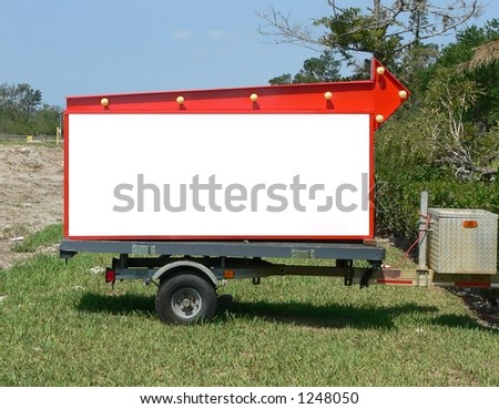 Marquis sign on a trailer on a roadside blank for copy.  The sign has an orange arrow pointing to the left.  The roadside a grassy area in a rural location and it is a cloudless, sunny day.