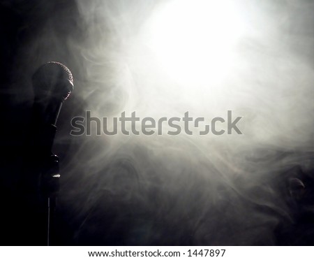 microphone standing to side of extremely smoky spotlight. The microphone is on the left side of the image and is backlit by the spotlight directed towards to viewer. The light is shining through fog