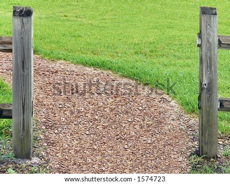 opening in split rail fence with mulch pathway leading to left