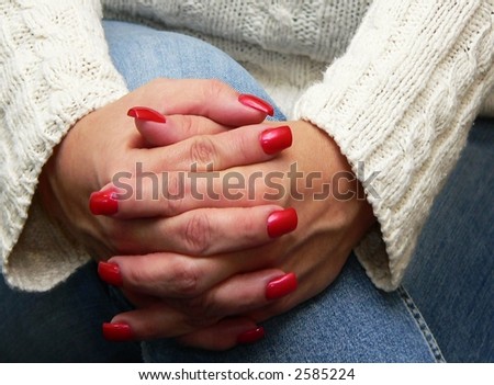 Woman\'s manicured hands clasped around her knee wearing jeans and a sweater
