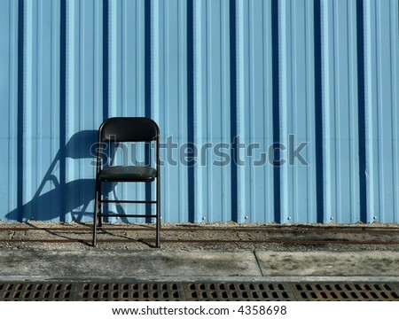 Single chair and shadow against blue building