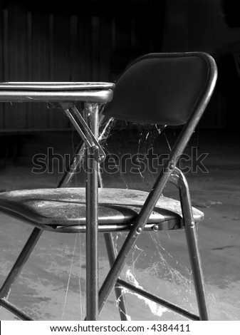 Black and white study of table and chair covered with dust and spider webs