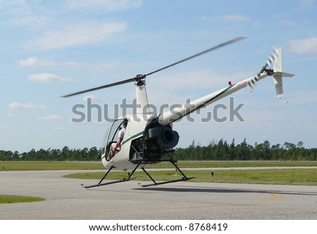 Small piston engine helicopter lifting off of tarmac