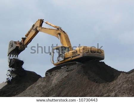 Construction hoe working atop a mound of dirt