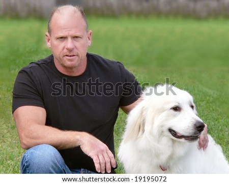 Middle aged man with his Great Pyrenees dog. The man is looking at the viewer and is dropped to one knee. He is wearing a black T-shirt and blue jeans. The dog is looking off camera to the right.