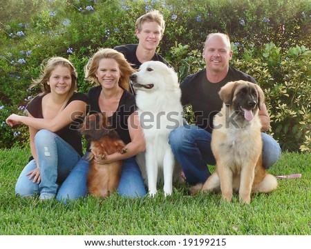 Attractive and happy family with their dogs sitting on a lawn.  The family consists of Mom, Dad, brother and sister.  They are dressed in matching black shirts with blue jeans.  It is a breezy day.