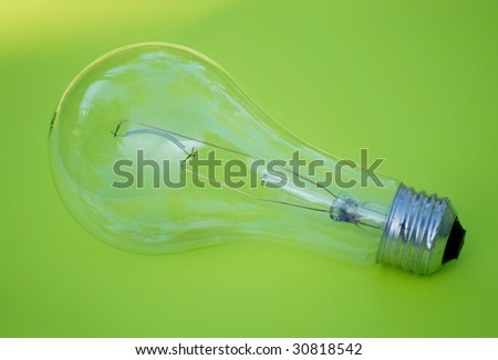 Green energy concept - un-powered incandescent light bulb on green background. The bulb is clear, not frosted. The filament is intact. The green background has a bright spot in the upper left corner.