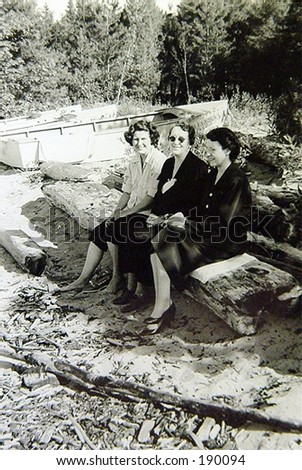 Sisters and mother on log at beach.  Two women wearing high heels.