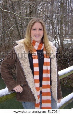 Pretty girl in wool lined coat & striped scarf leaning on snowy  bridge. Dental appliance evident.