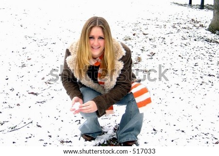 Pretty girl in wool lined coat, jeans & striped scarf making a snowball. Dental appliance evident.