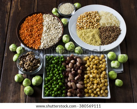 Vegan sources of protein: grains, lentil, beans, nuts and Brussels sprouts on a dark wooden table