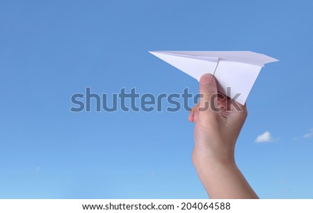 Paper airplane in children hand over sunny summer blue sky