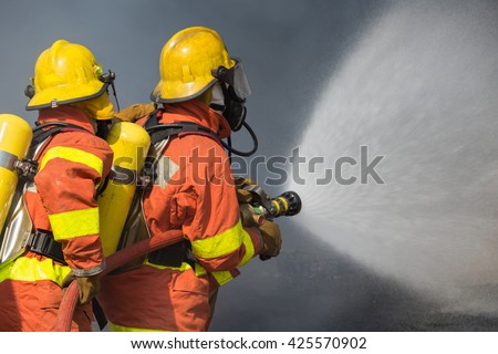 2 firefighters spraying water in fire fighting with dark smoke background