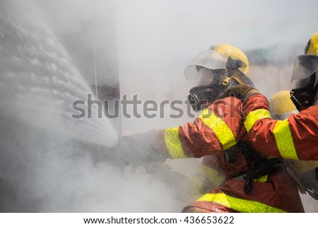 two firemen in oxygen mask helmet and fire fighting suit spraying water to fire surround with smoke and drizzle